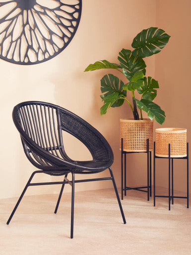 Black wicker chair in a room with a plant and baskets on a light wood floor.