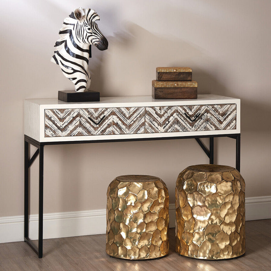 Console table with decorative zebra statue and stacked books, accompanied by two gold stools.