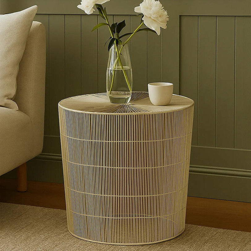 Wicker side table with a vase of flowers and a cup against a green wall.