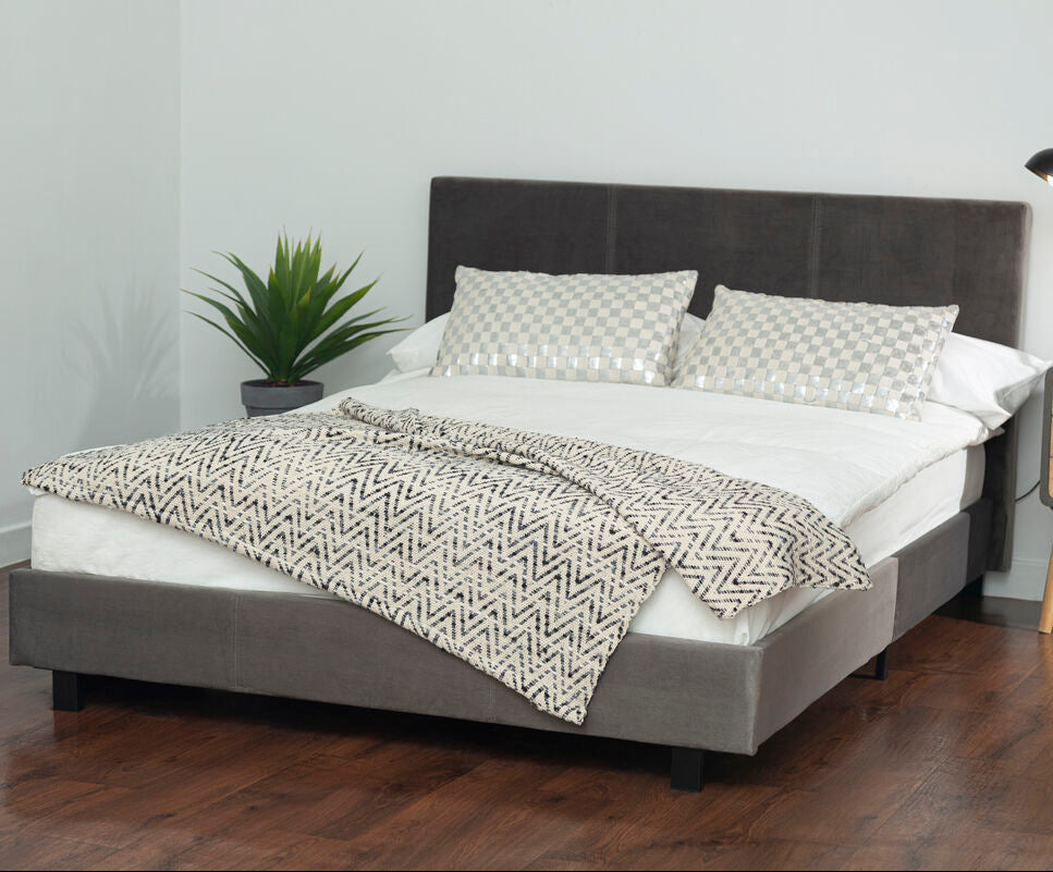 Gray upholstered bed with white bedding and a patterned throw in a bedroom setting.
