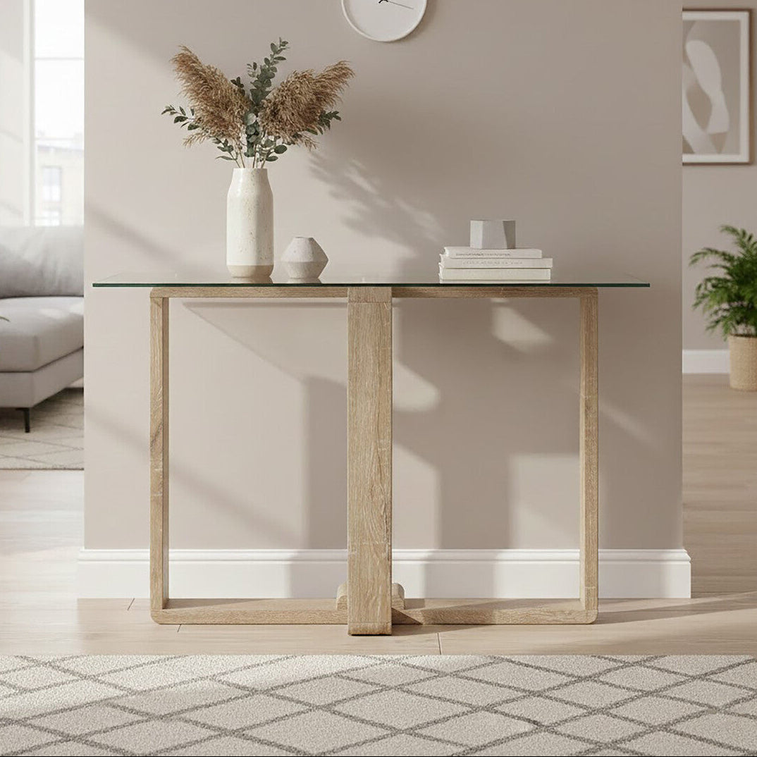 Modern living room with a glass-top table, vase with dried plants, and books against a neutral wall.
