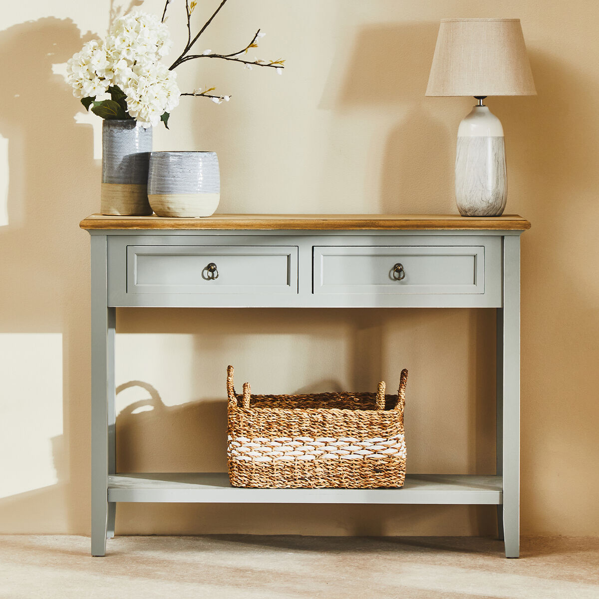 Console table with drawers, a basket, and decorative items against a beige wall.