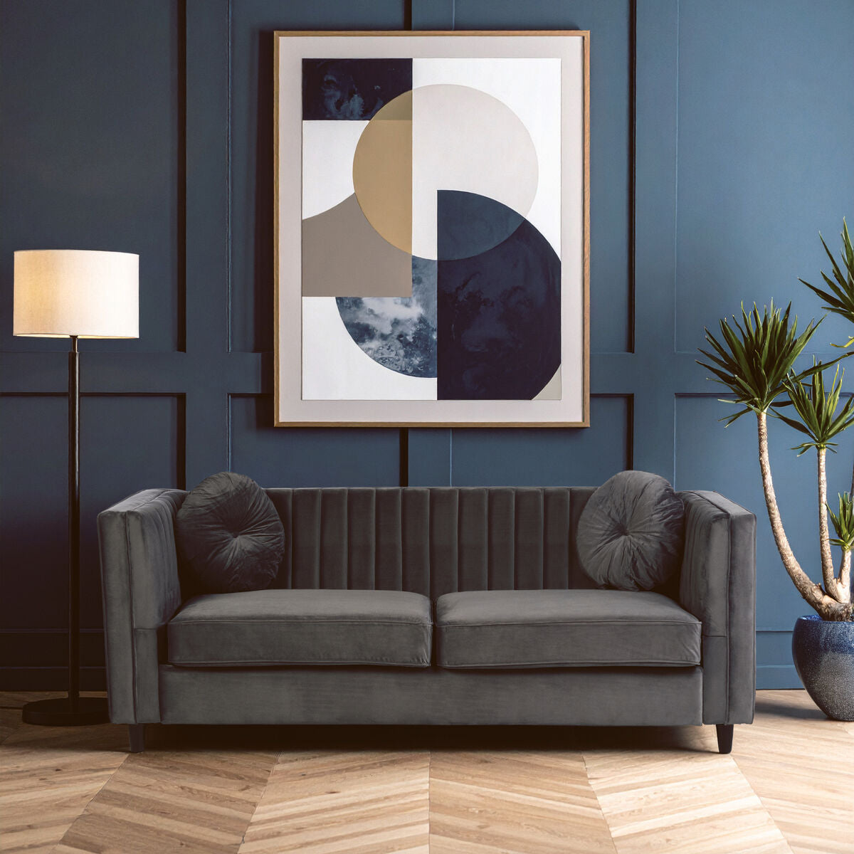 Gray sofa in a room with abstract art, lamp, and plant against a blue wall.