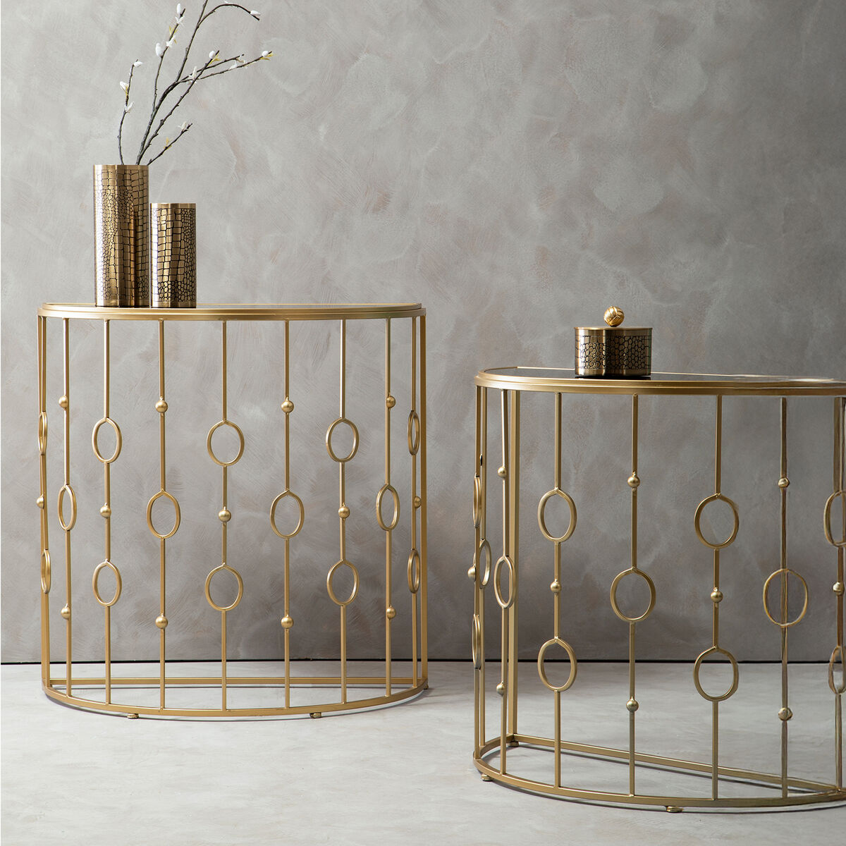 Two gold metal side tables with decorative patterns against a gray wall.