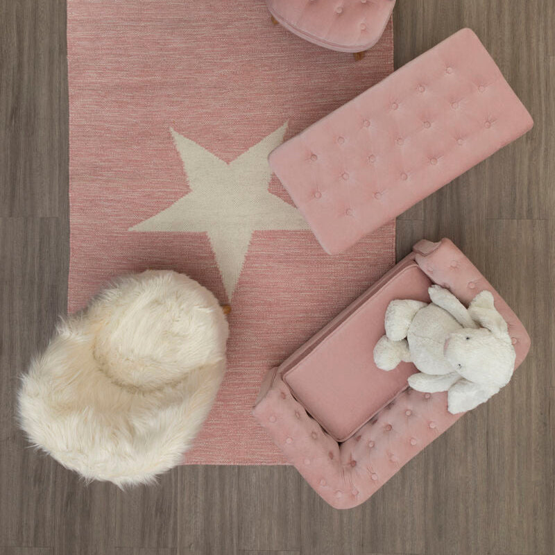 Pink rug with star design on a wooden floor, surrounded by plush toys and furniture.