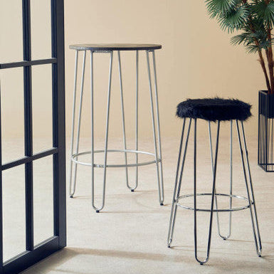 Two bar stools with metal legs and a fur-covered stool in a room with a plant and window.