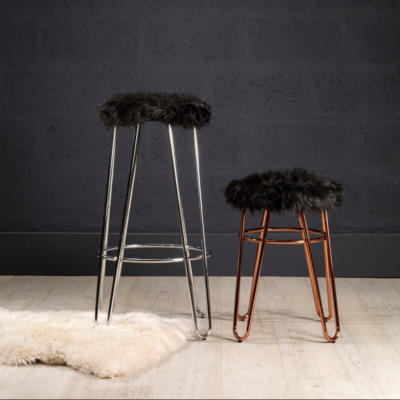 Two bar stools with fur seats on a wooden floor against a dark wall.