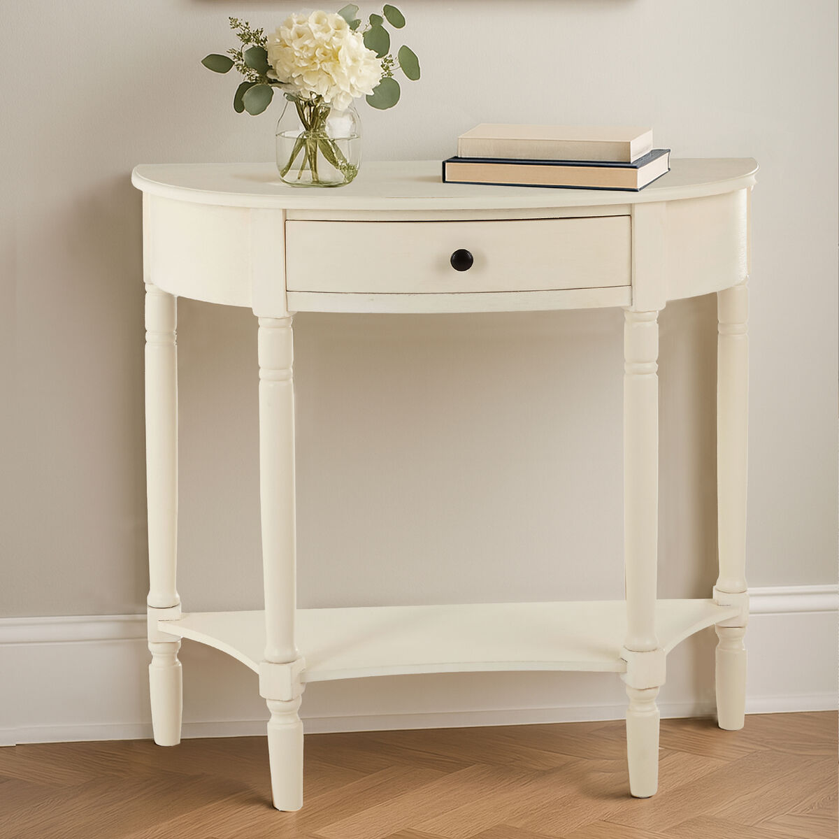 White side table with a vase of flowers and books on a wooden floor.