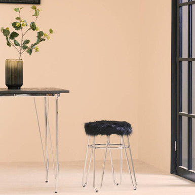 Modern stool with black fur top next to a glass table against a beige wall.