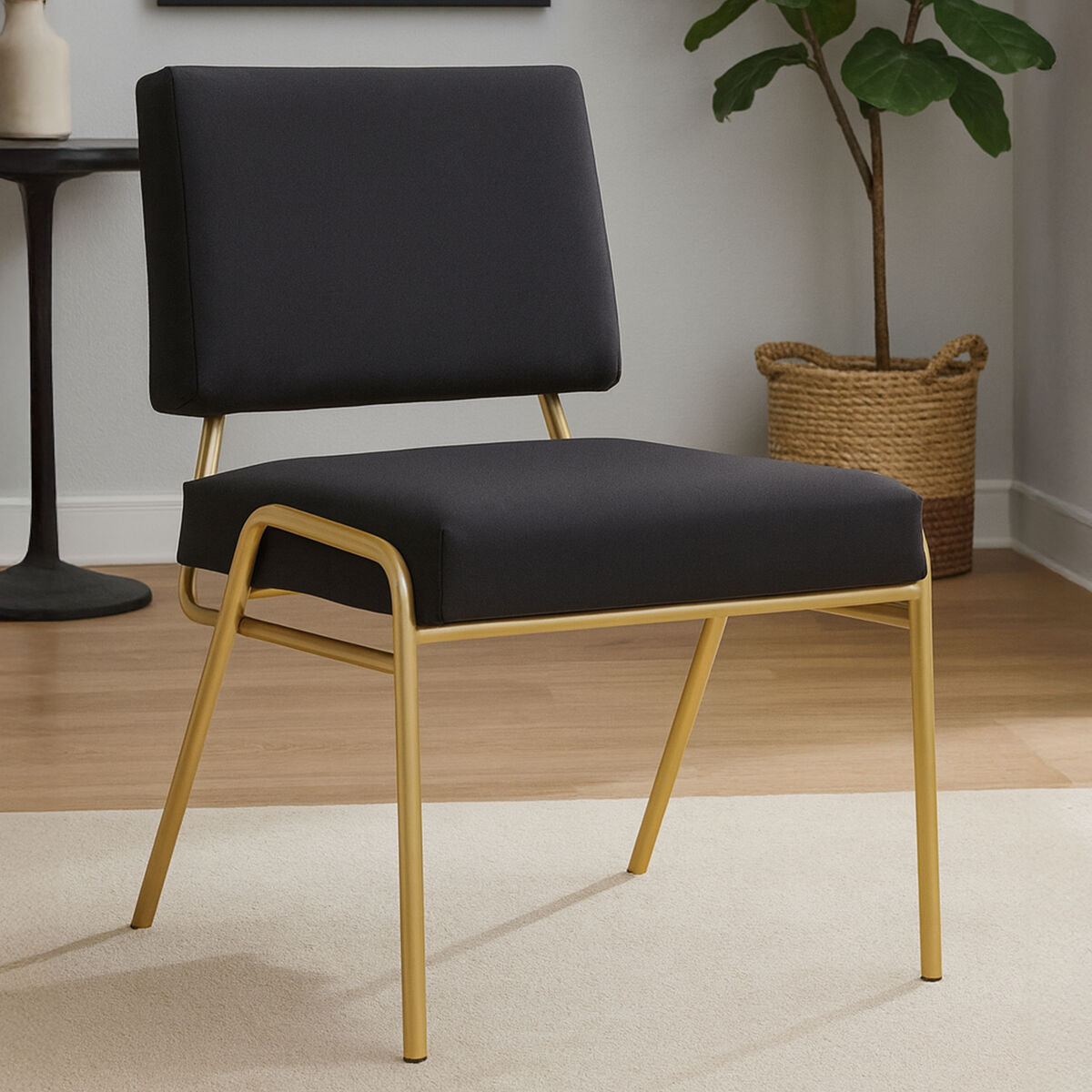 Black chair with gold frame in a room setting with a plant and table.
