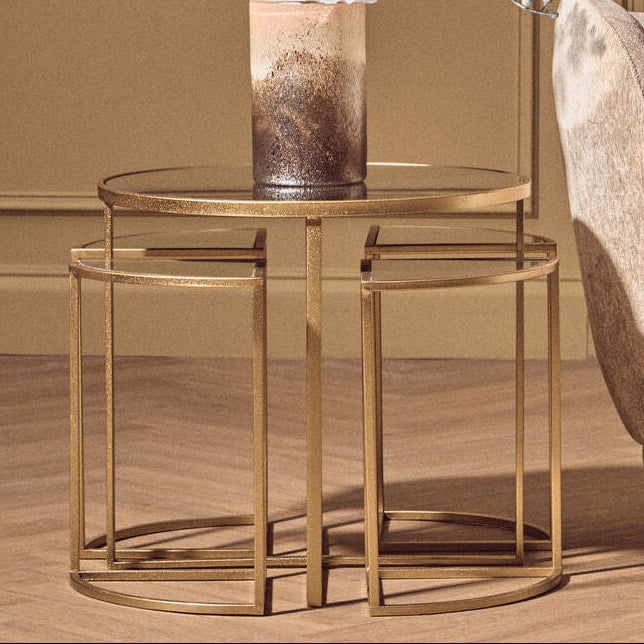 Gold side table with a vase and flowers next to a beige armchair in a room with brown walls.