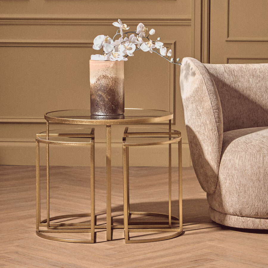 Gold side table with a vase and flowers next to a beige armchair in a room with brown walls.