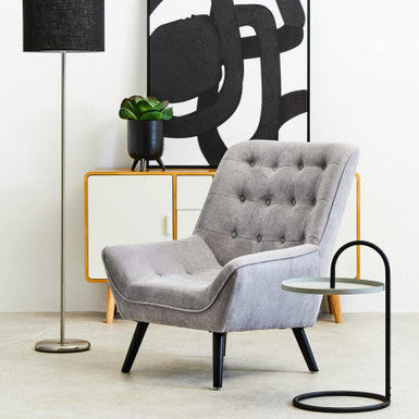 Gray armchair in a modern living room with abstract art and floor lamp.