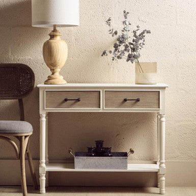 Small wooden console table with two drawers, a lamp, and decorative items against a beige wall.
