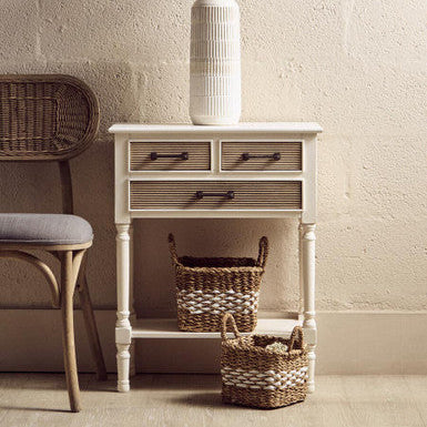 White side table with drawers and a vase on a light-colored floor against a white wall.