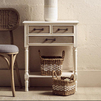 White side table with drawers and a vase on a light-colored floor against a white wall.