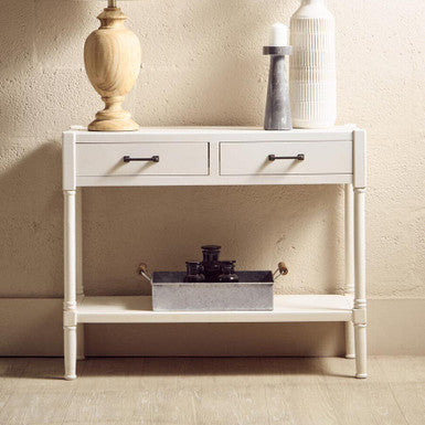 White console table with a lamp, vase, and decorative items against a beige wall.