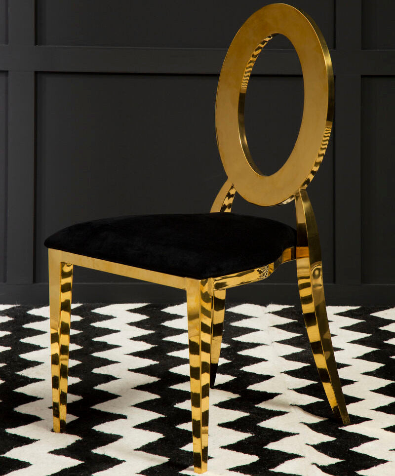 Gold chair with black cushion on a black and white patterned rug against a dark wall.