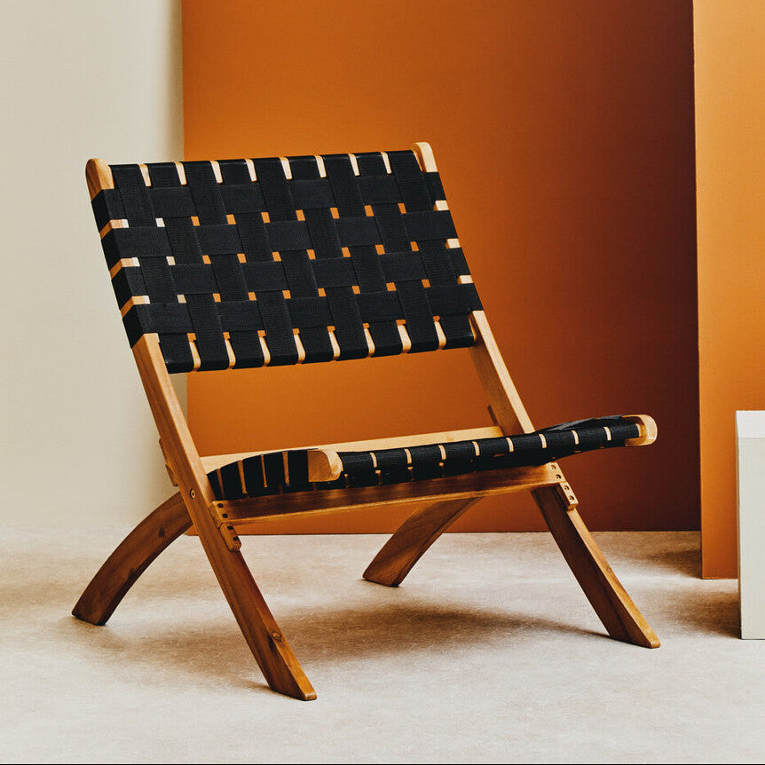 Wooden chair with black woven backrest against an orange wall