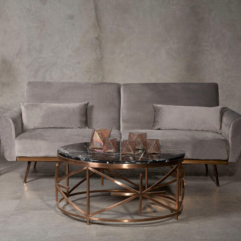 Gray sofa with bronze coffee table and side table against a concrete wall.