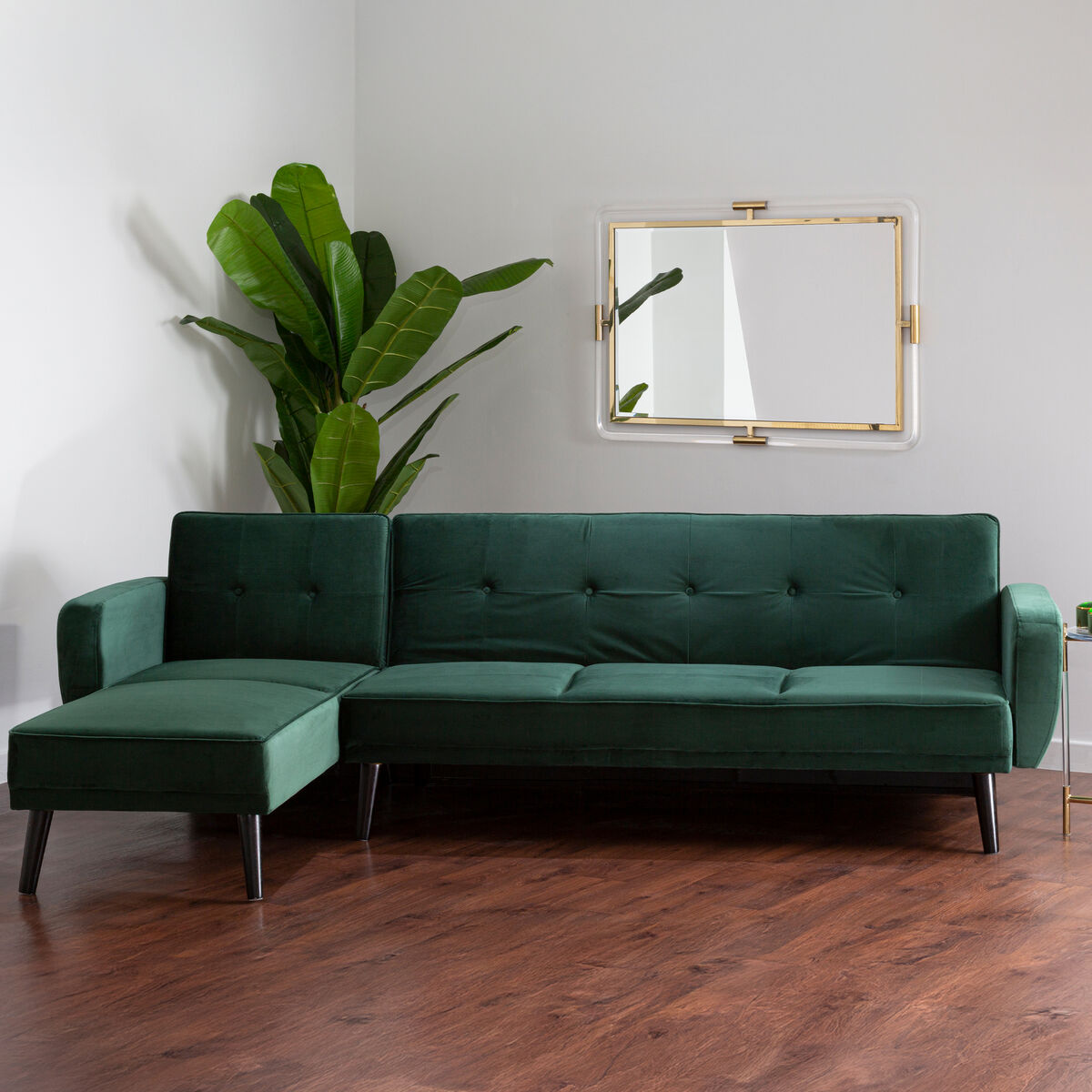 Green sectional sofa in a room with a plant and mirror on the wall.