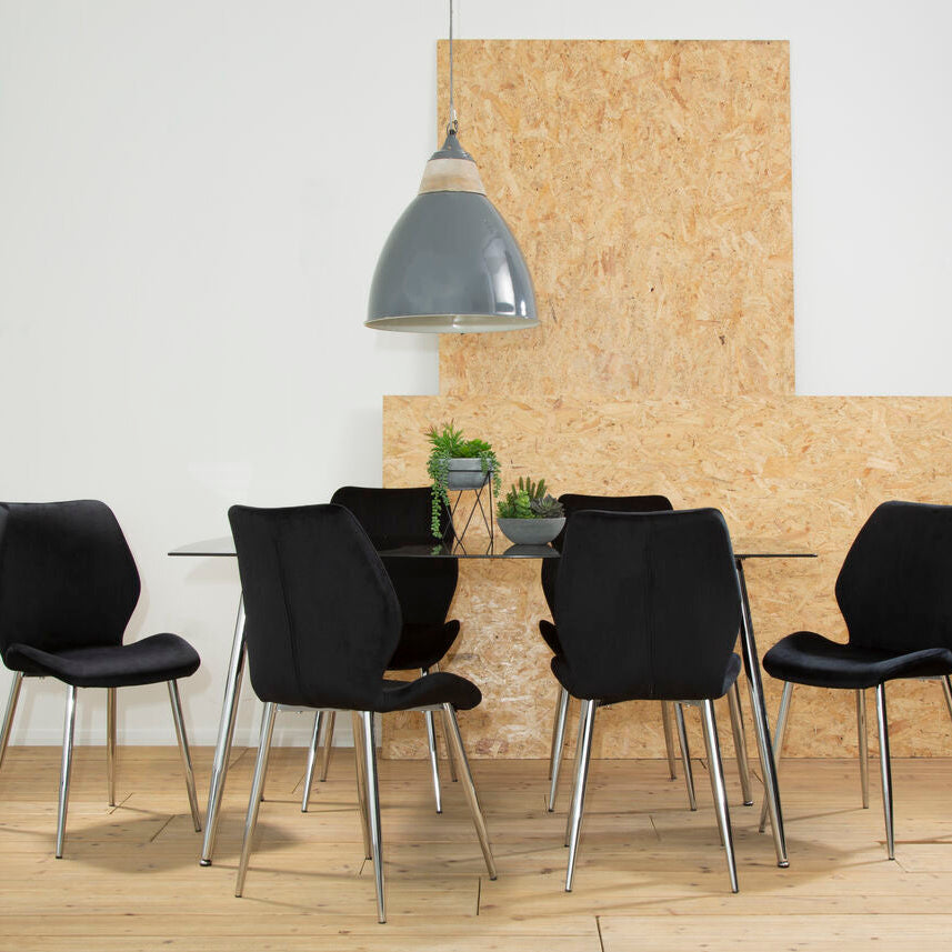 Dining area with black chairs around a glass table against a wooden wall.