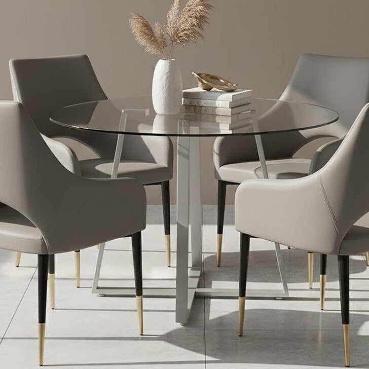 Dining room with a round glass table and four chairs against a beige wall with abstract art.