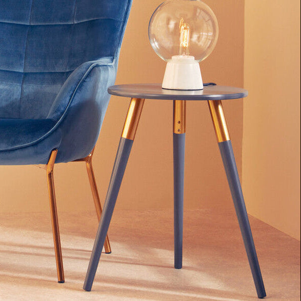 Blue velvet chair and small table with a lamp against a beige wall