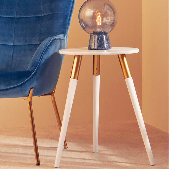 Blue upholstered chair next to a small round table with a decorative lamp against a beige wall.
