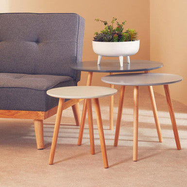 Gray sofa with three wooden side tables and a plant on a beige background