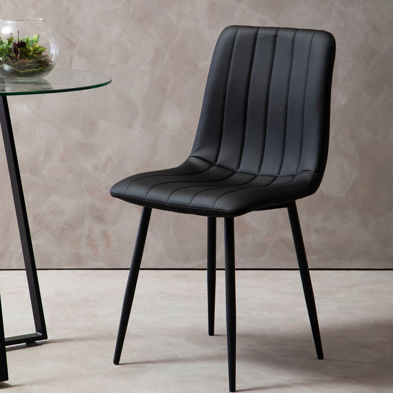 Black chair in a room with a gray wall and glass table.