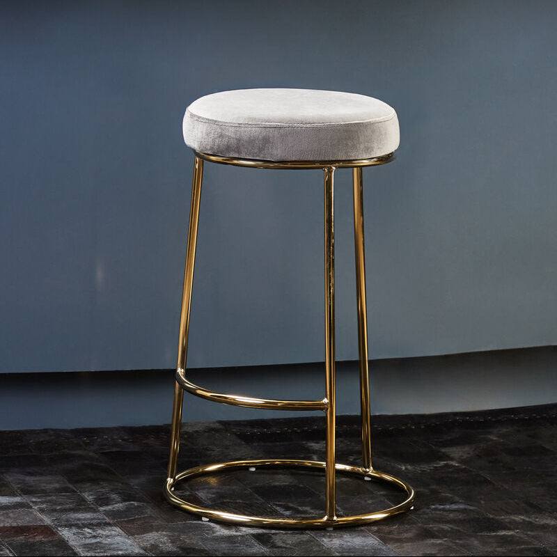 Bar stool with gold legs and gray cushioned seat in front of a blue wall.