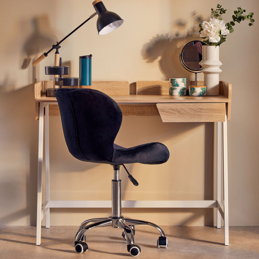 Wooden desk with black office chair and decorative items against a beige wall.