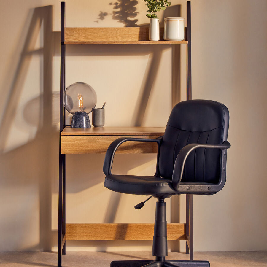 Black office chair in front of a wooden desk with shelves.