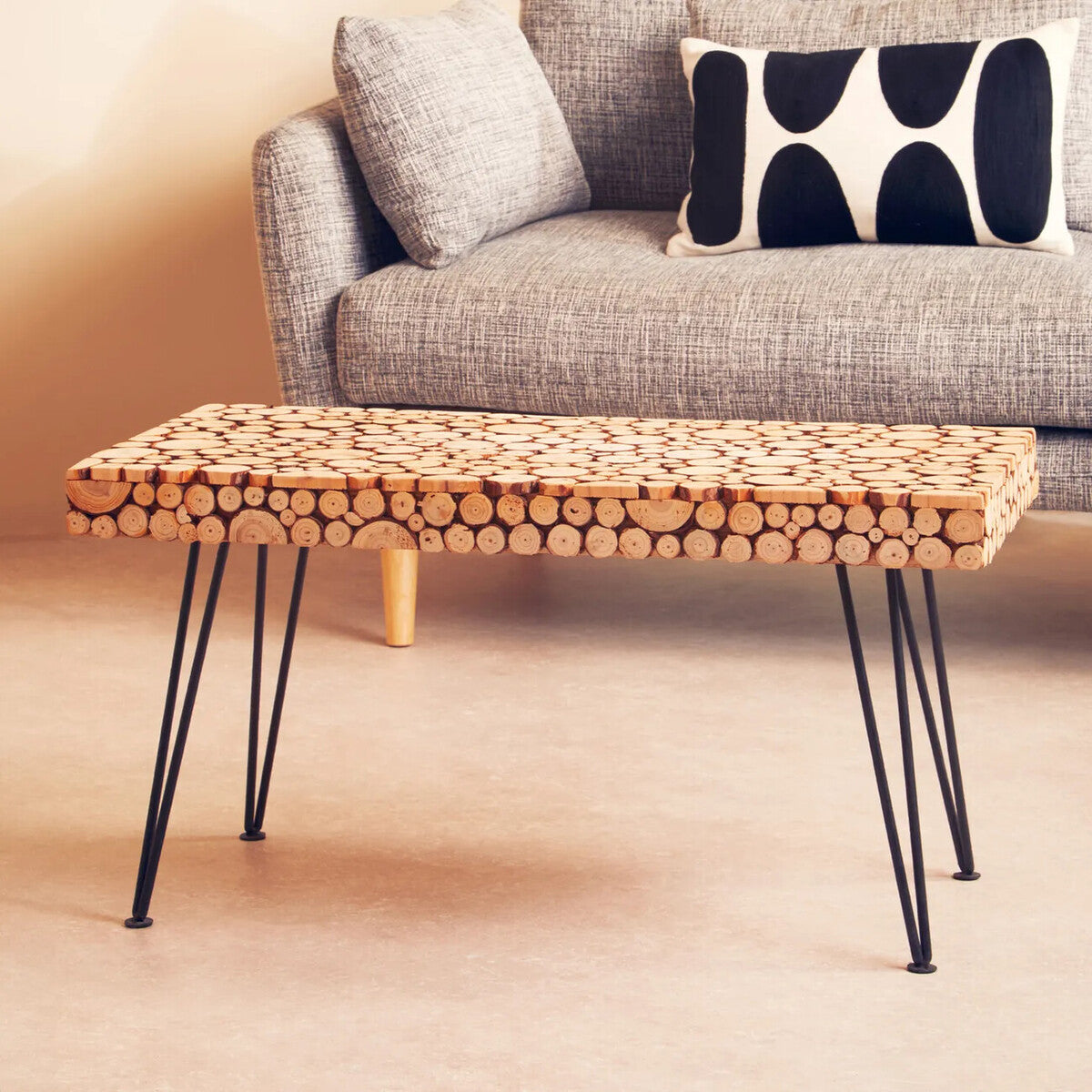 Wooden coffee table with black hairpin legs in front of a gray sofa with decorative pillows.