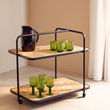 Two-tiered serving cart with green glasses and a pitcher on a neutral background