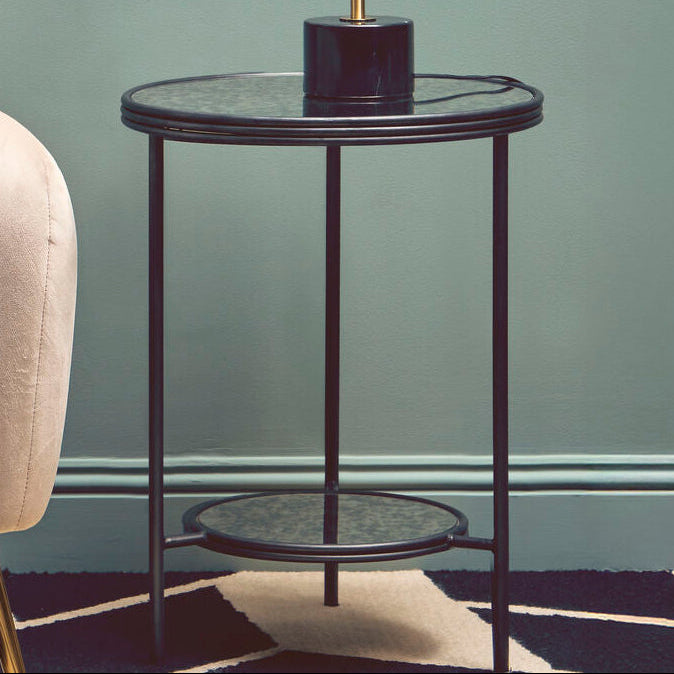 Modern living room with a beige armchair, round glass table, and gold lamp.