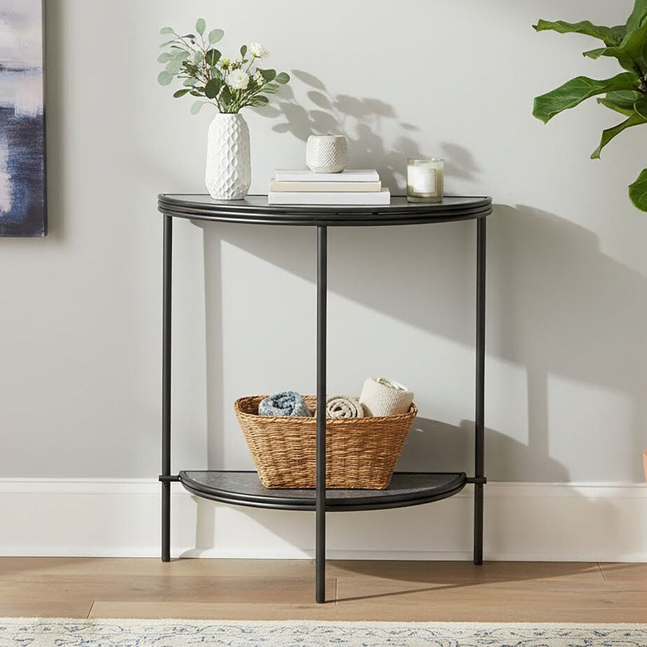 Small round black metal table with decorative items in a room with a plant and abstract art.