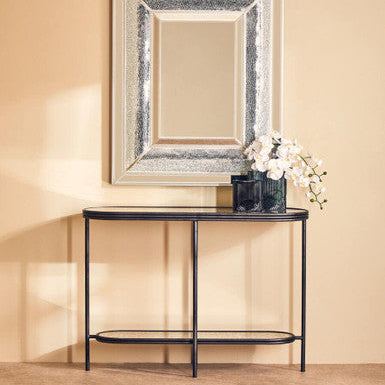 Decorative mirror with a black console table against a beige wall
