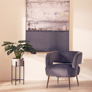 Gray armchair in a room with a large abstract painting on the wall and a potted plant.