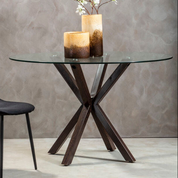 Modern glass dining table with dark wooden legs and a black chair against a gray wall.