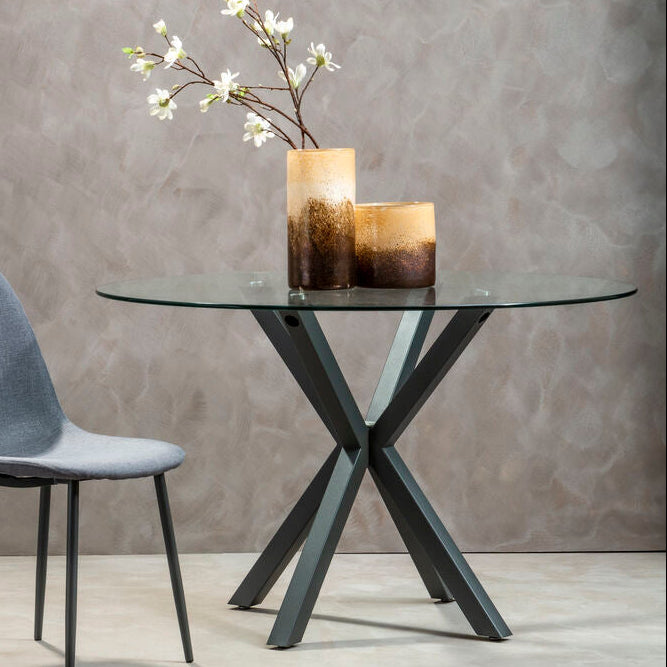 Modern glass dining table with metal legs and a gray chair against a gray wall.