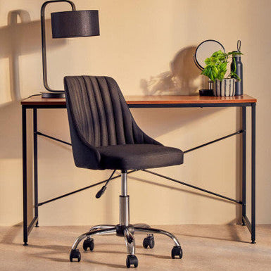 Modern office desk with black chair, lamp, and decorative items against a beige wall.