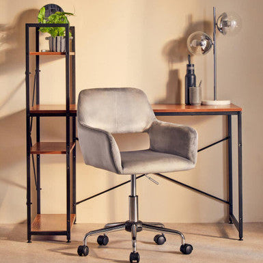 Gray office chair in front of a wooden desk with a bookshelf and lamp in a room.