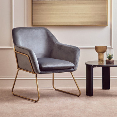 Modern gray chair with gold legs in a room with a abstract painting on the wall.