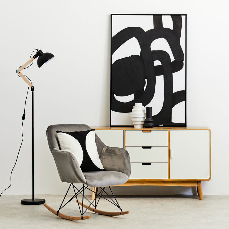 Modern interior with a rocking chair, floor lamp, and abstract art on a white wall.