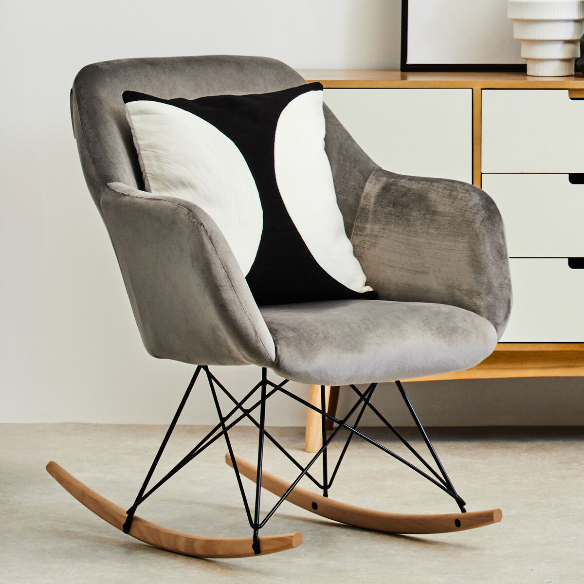 Gray rocking chair with a black and white pillow in a modern room.