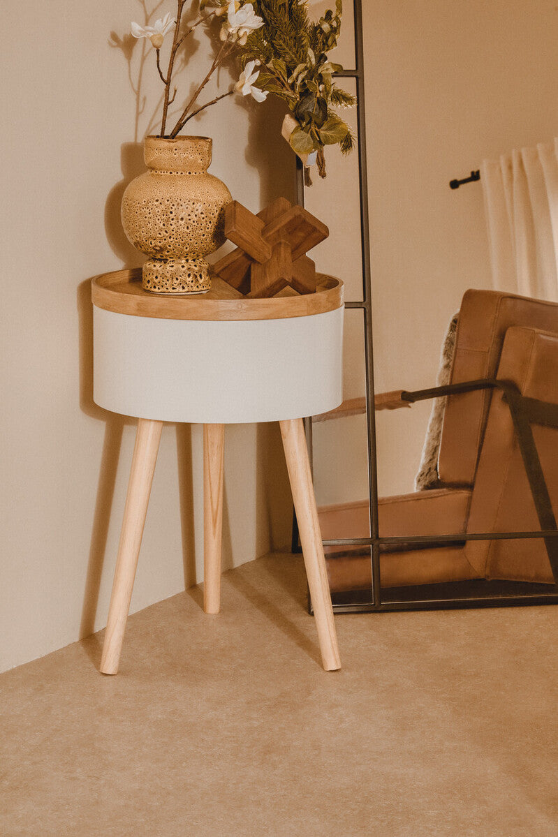 Small round side table with a textured vase and wooden cross on a beige carpet.