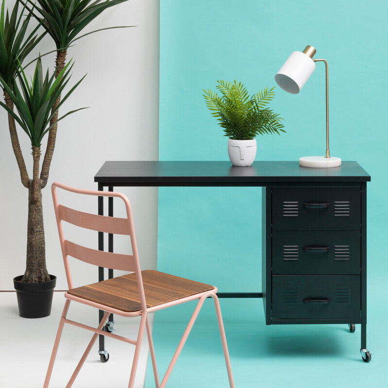 Modern office setup with a black desk, pink chair, and green plants against a teal wall.
