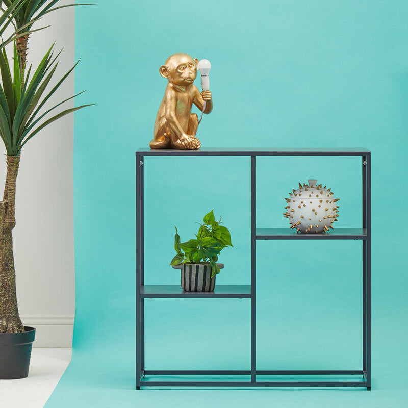 Decorative shelf with a gold monkey figurine, potted plant, and clock against a turquoise wall.